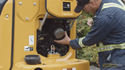 heavy duty mechanic pulls out a filter on a John Deere mini excavator