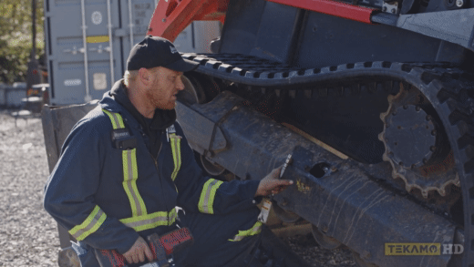 Heavy mechanic points out where to find graease valve on a Kubota skid steer