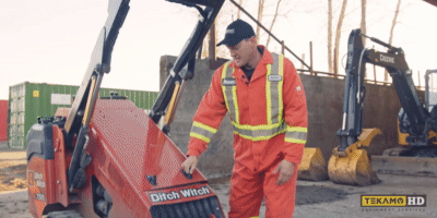 Heavy duty mechanic opening the hood of a Ditch Witch SK755