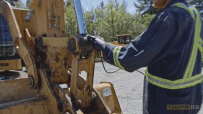 Heavy equipment mechanic shows where to grease the moving parts of an excavator