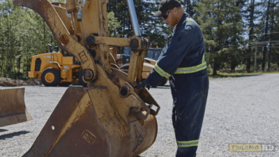Heavy equipment mechanic points to the excavator pins for greasing